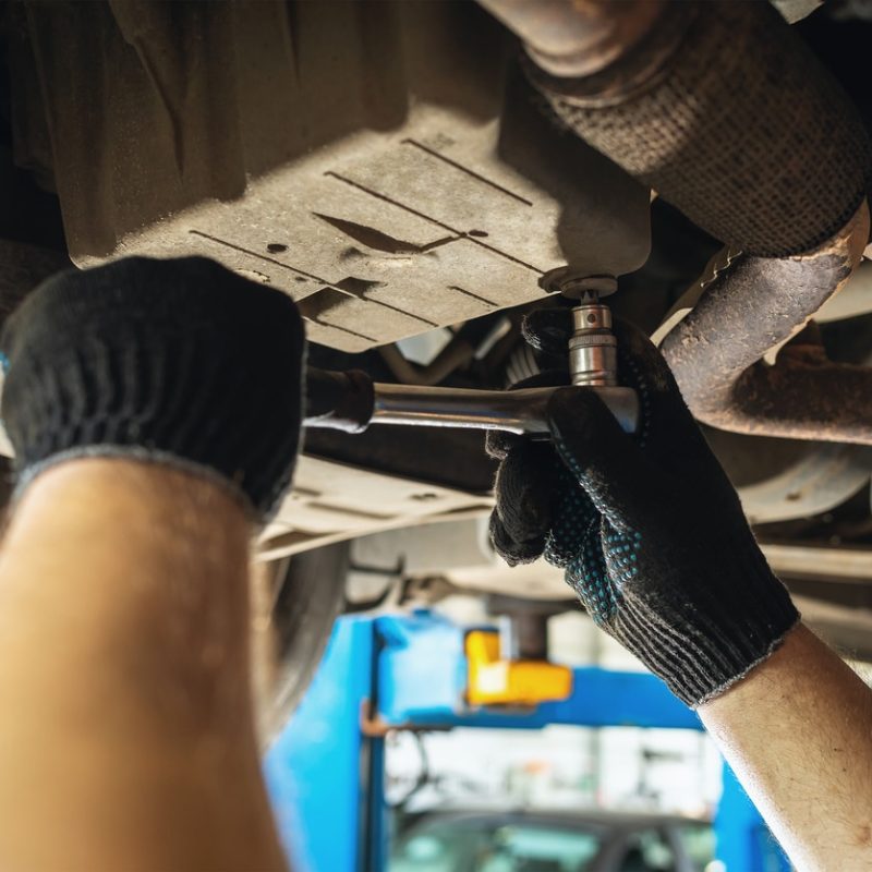Un garagiste dévisse un élément du dessous d'une voiture